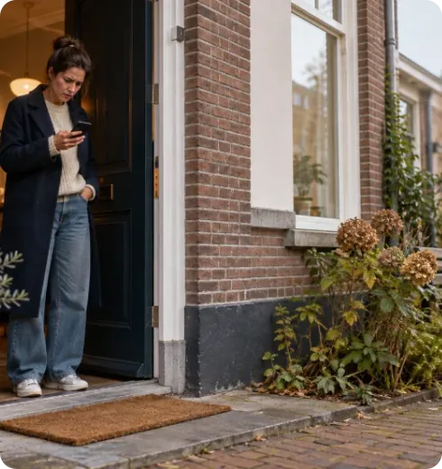 Vrouw kijkt bij haar voordeur op haar telefoon naar de bezorgstatus van haar pakket.